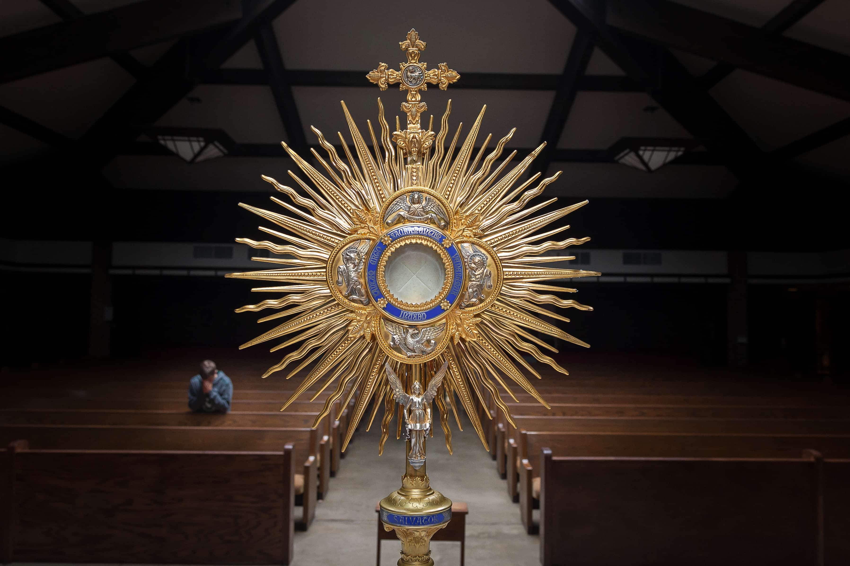 Monstrance with consecrated host in it with man kneeling in background